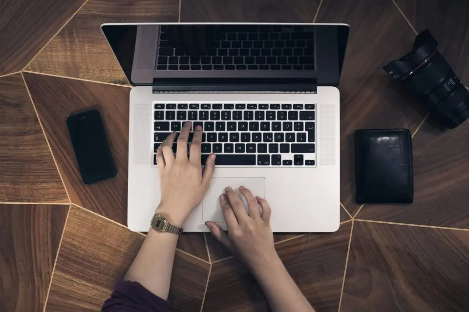 Person arbeitet von oben gesehen an einem Laptop auf einem Holztisch